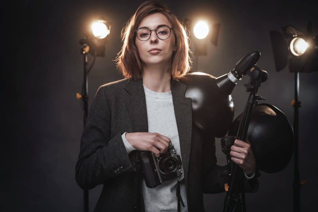 Beautiful redhead female photographer holds a digital camera and looking on the camera