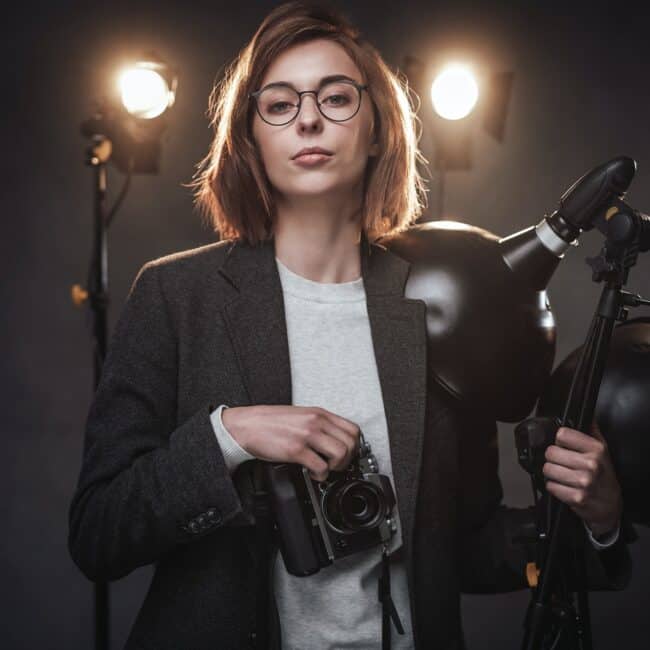 Beautiful redhead female photographer holds a digital camera and looking on the camera