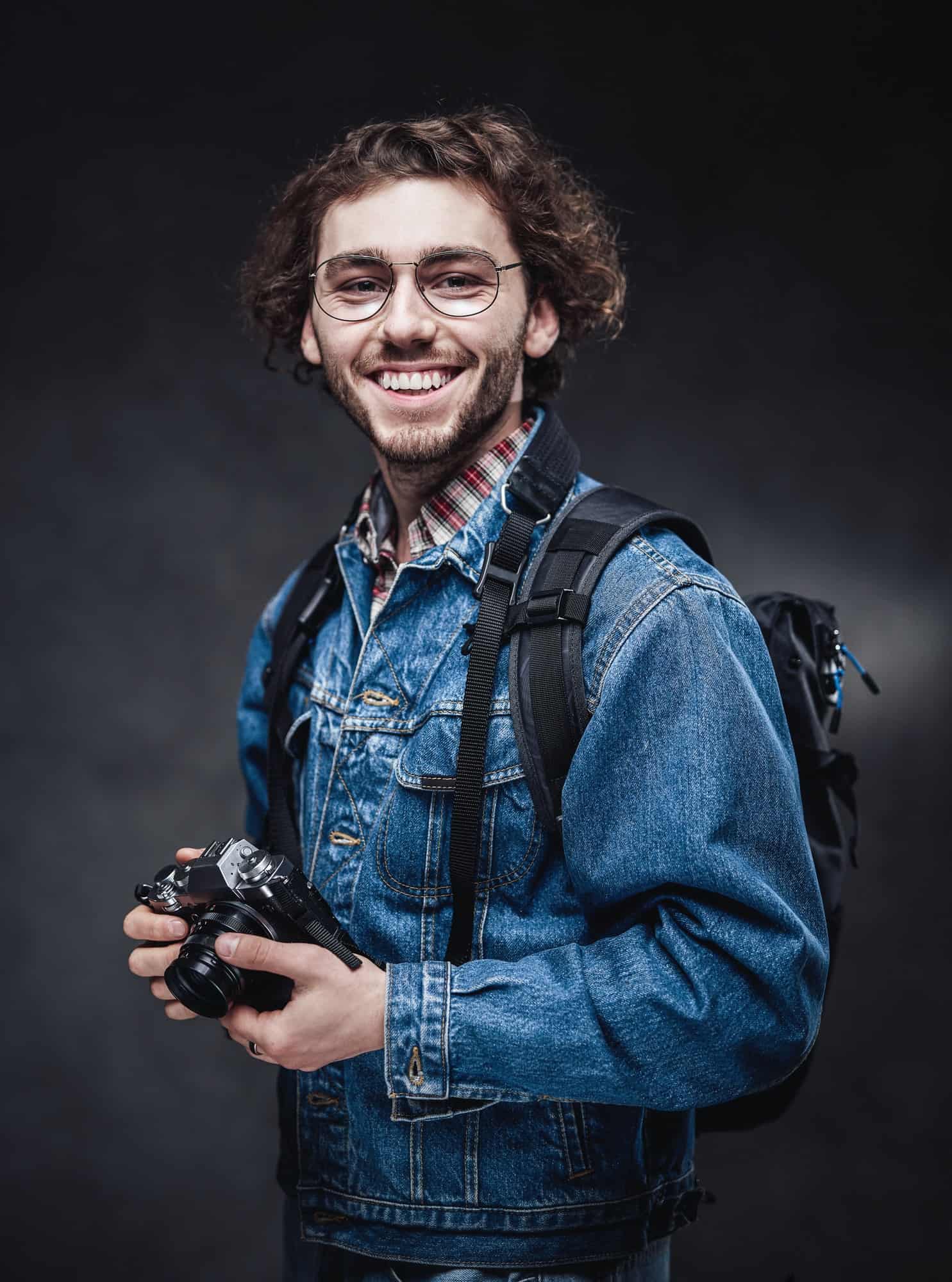 Portrait of a handsome young photographer with curly hair wearing denim jacket holds a camera