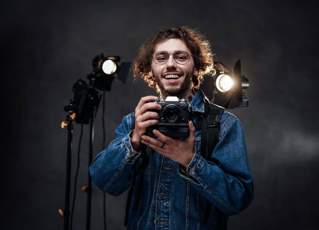 Young photographer holds a camera. Studio portrait with lighting equipment in the background