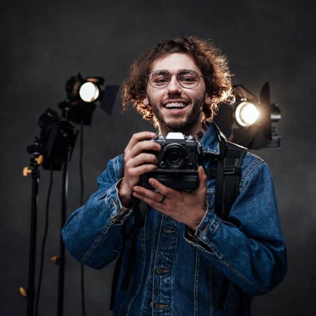 Young photographer holds a camera. Studio portrait with lighting equipment in the background